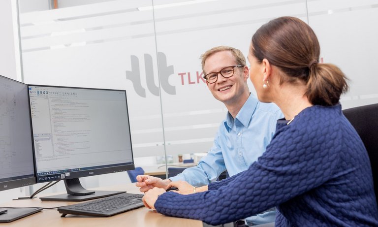 Foto von zwei Mitarbeitenden am Schreibtisch Foto von zwei Mitarbeitenden am Schreibtisch in einem modernen Büro, die eine technische Simulation an zwei Monitoren besprechen.